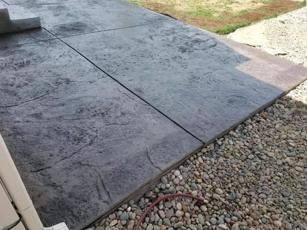Dark slate stamped concrete patio edged with river rock in Colorado Springs
